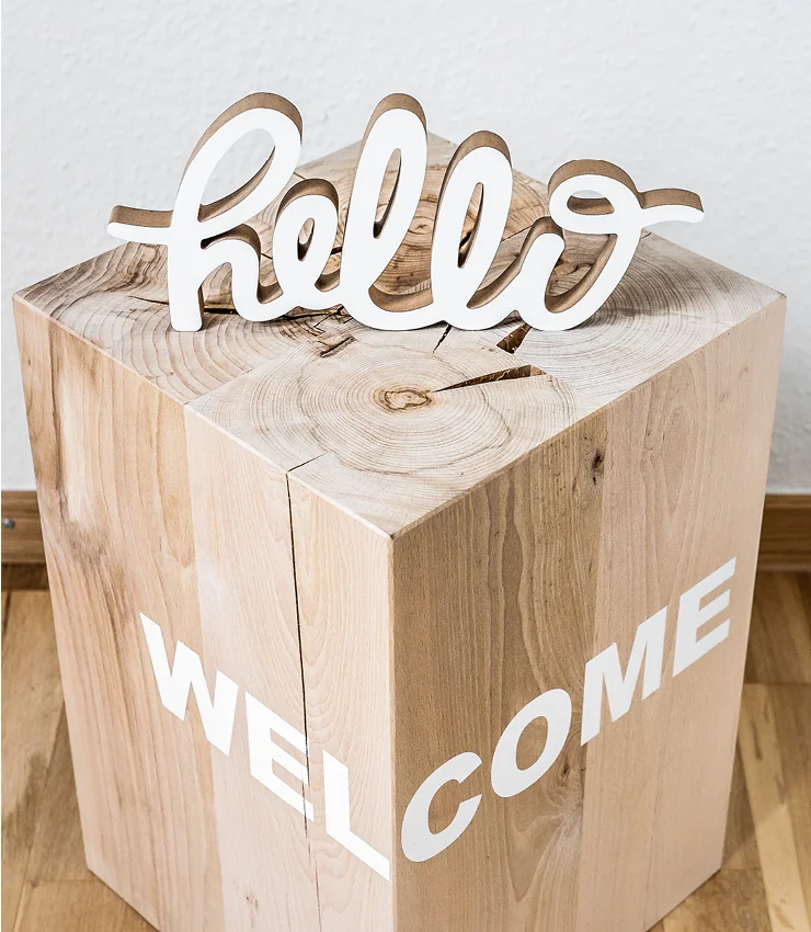 Hölzerner Schriftzug „Hello“ auf einem Holzblock als Willkommensgruß